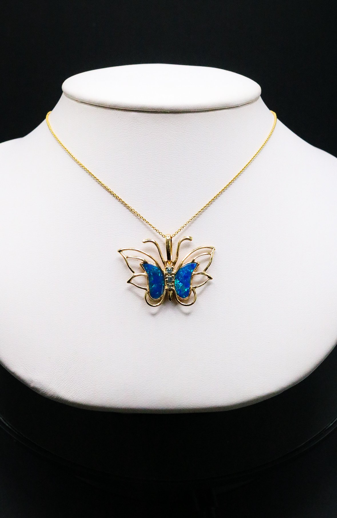 Gold butterfly pendant with blue opal wings on a gold chain, displayed on a necklace bust