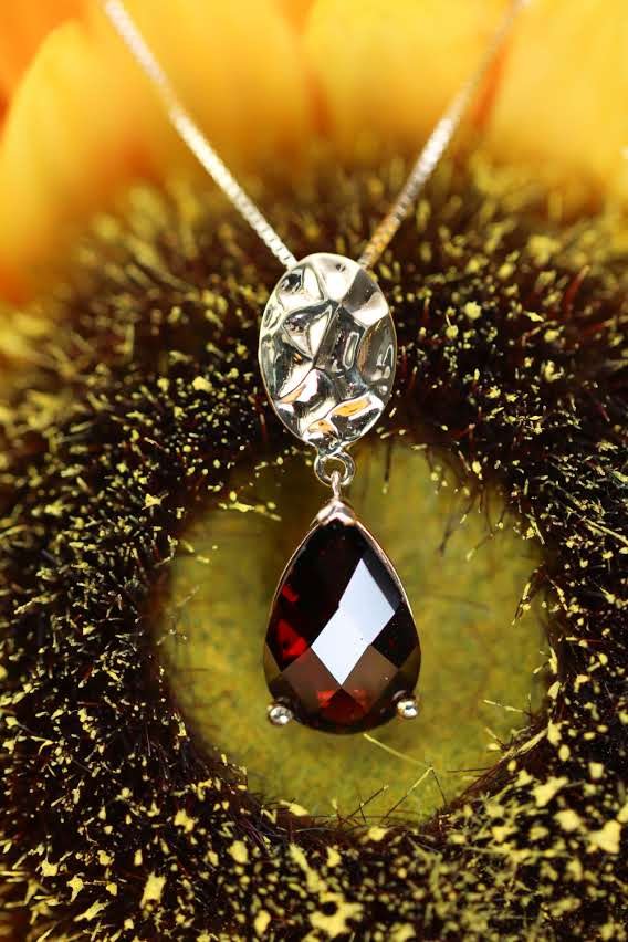 Teardrop garnet pendant with hammered silver bail, photographed in a sunflower center