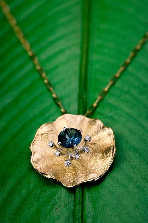 Gold lily pad pendant with blue topaz and scattered natural diamonds on a green leaf