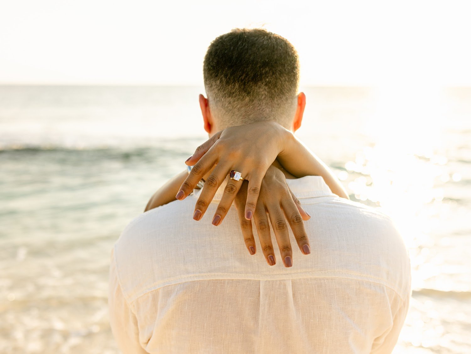 Customer photo: couple on the beach, her hand showing the custom engagement ring, from Leena's Google review