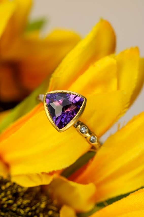Trillion-cut amethyst ring in gold bezel setting among yellow sunflower petals
