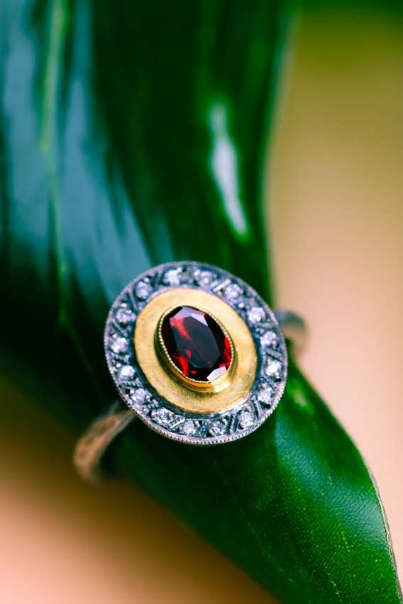Oval garnet ring framed in gold with a diamond halo, photographed on a leaf