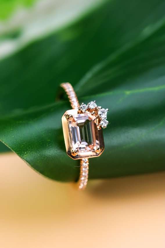 Emerald-cut morganite ring with diamond cluster on a pavé rose gold band, set against a leaf