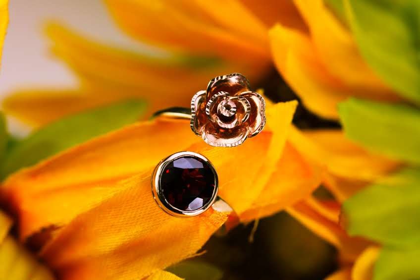 Open ring with a sculpted rose and round garnet, nestled among sunflower petals