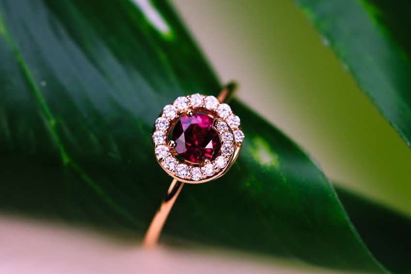 Rose gold ring with a rich tourmaline center and natural diamond halo, resting on a green leaf