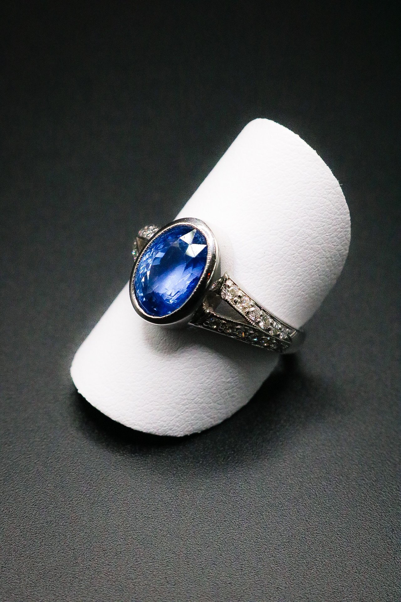 Oval blue sapphire ring with split diamond band in white gold, studio photograph