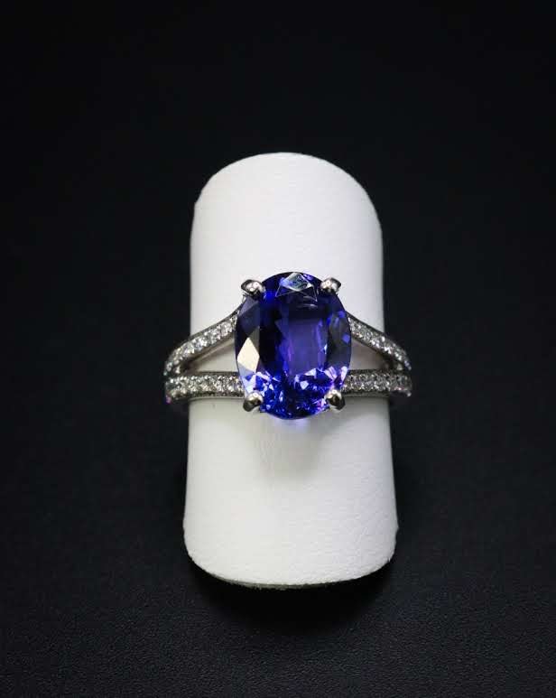 Oval blue sapphire ring with split natural diamond shank, studio photograph on white ring stand