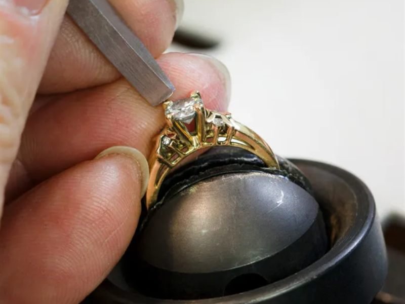 A jeweler holding a diamond ring against a bench block while making a repair