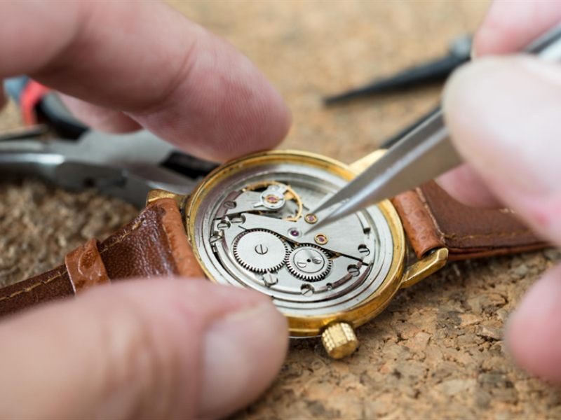 A watchmaker working on an open watch movement with tweezers
